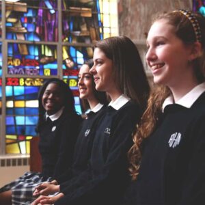 girls in uniform in a pew by a stained glass window